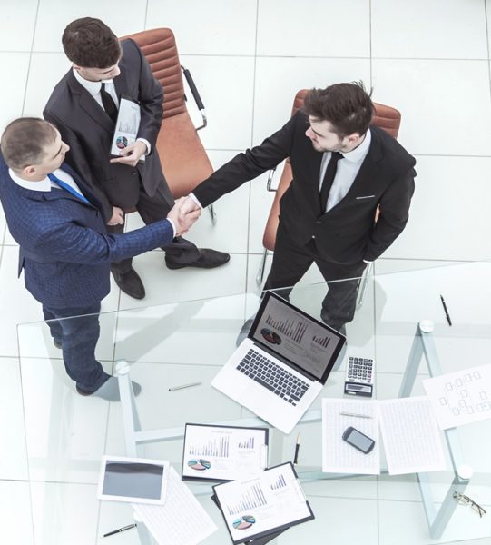top view - handshake of business partners before considering a new financial agreement near the desktop